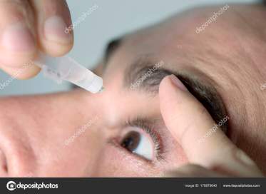 closuep of a young caucasian man applying eye drops to his eyes